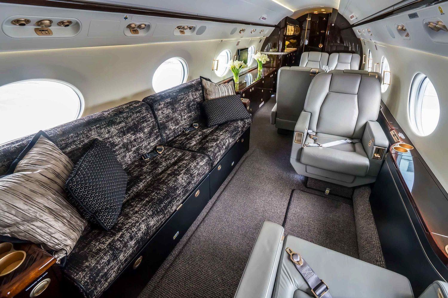 Business jet cabin with grey leather chairs, dark patterned sofa and bespoke curtains