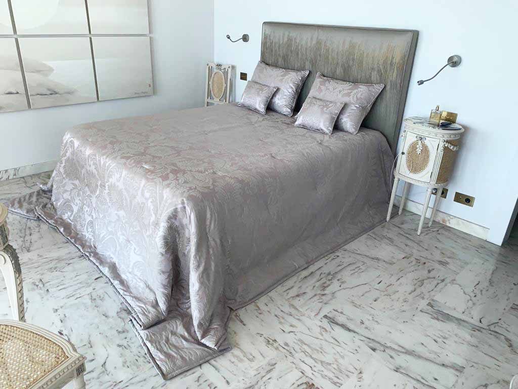 Bedroom dressed with a quilted silver damask bedspread and matching cushions