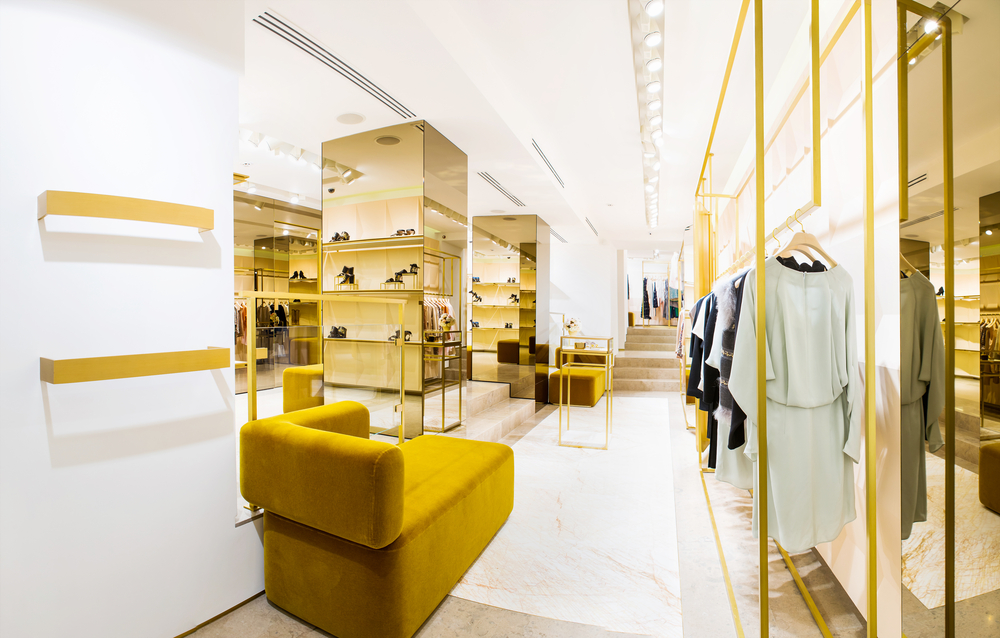Fashion boutique with gold metalwork display structures, mustard velvet banquette and ready-to-wear racks