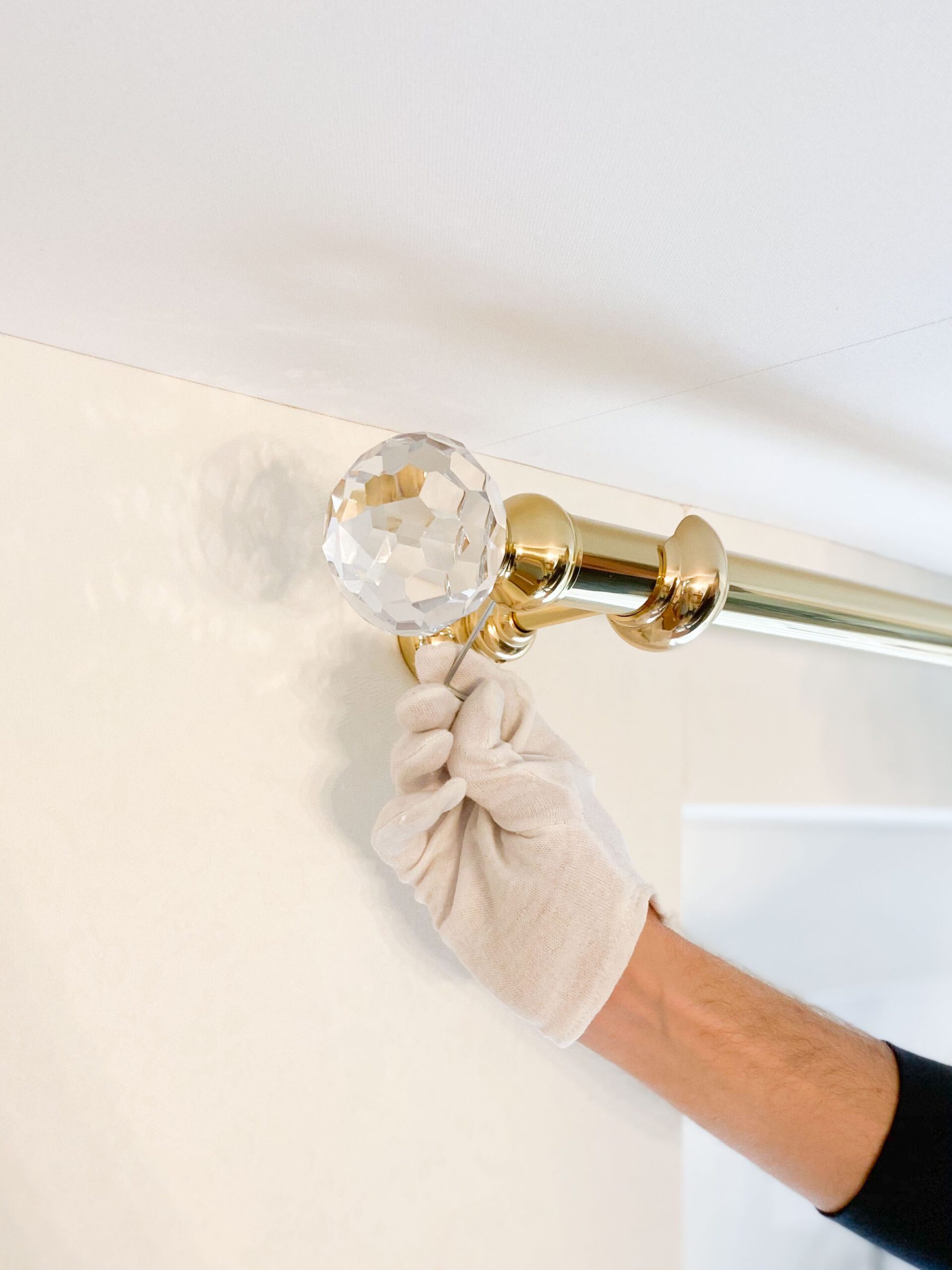 Gloved hand fitting a brass curtain rod with a crystal finial